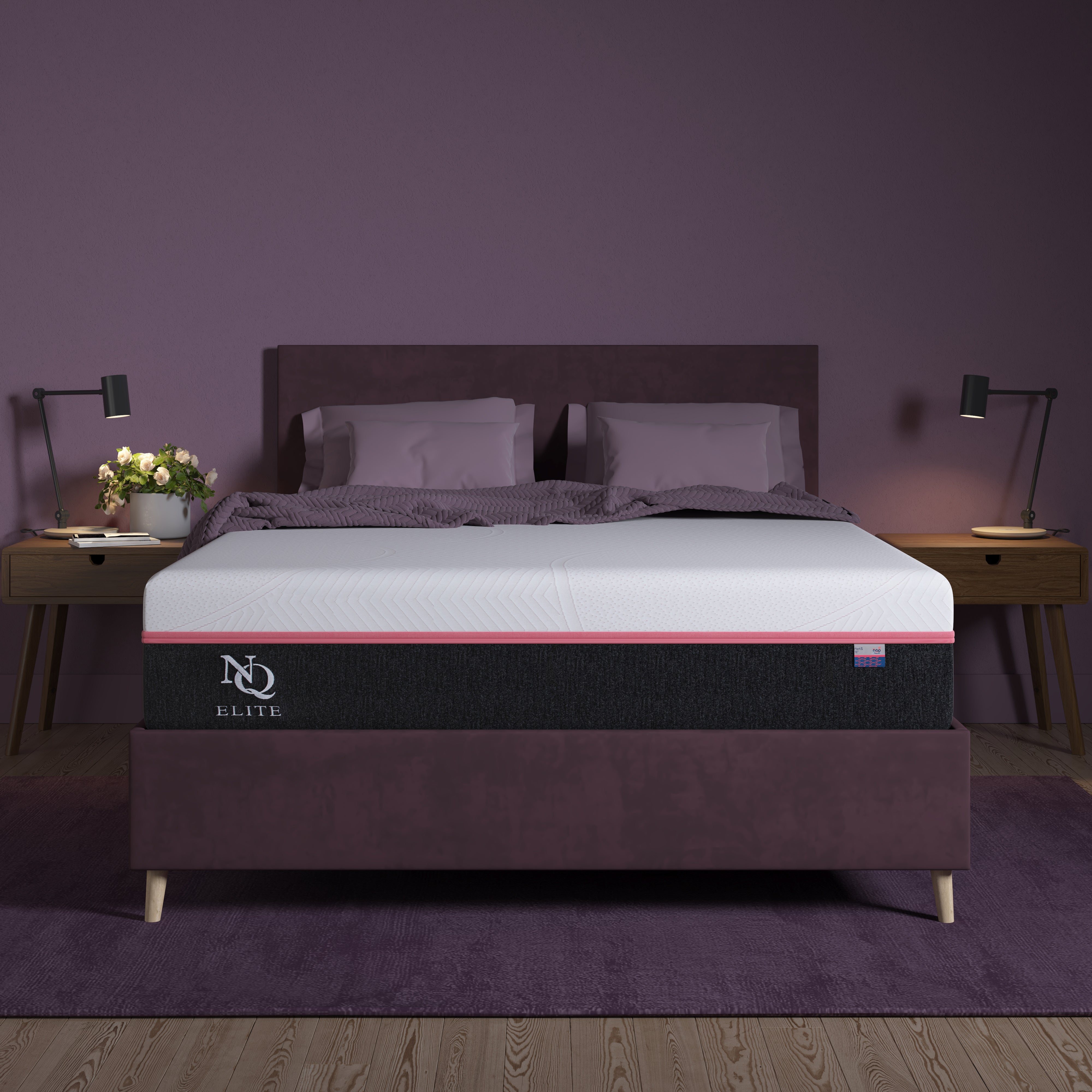 An Elite Series Mark Latex Foam Mattress by NapQueen, shown in a bedroom setting with a dark headboard and gray bedding, illuminated by bedside lamps.
